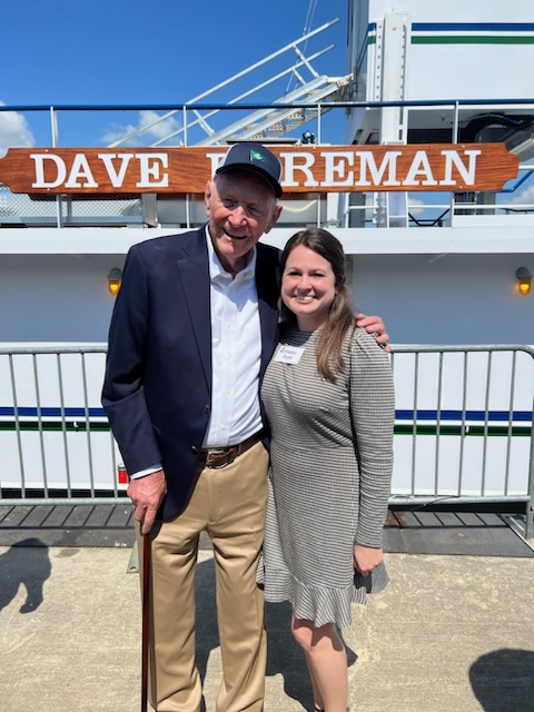 A picture of Dave Foreman and Shelby Ryals in front of a boat named after him in honor of his work with AccuTRANS and influence on the entire maritime industry.